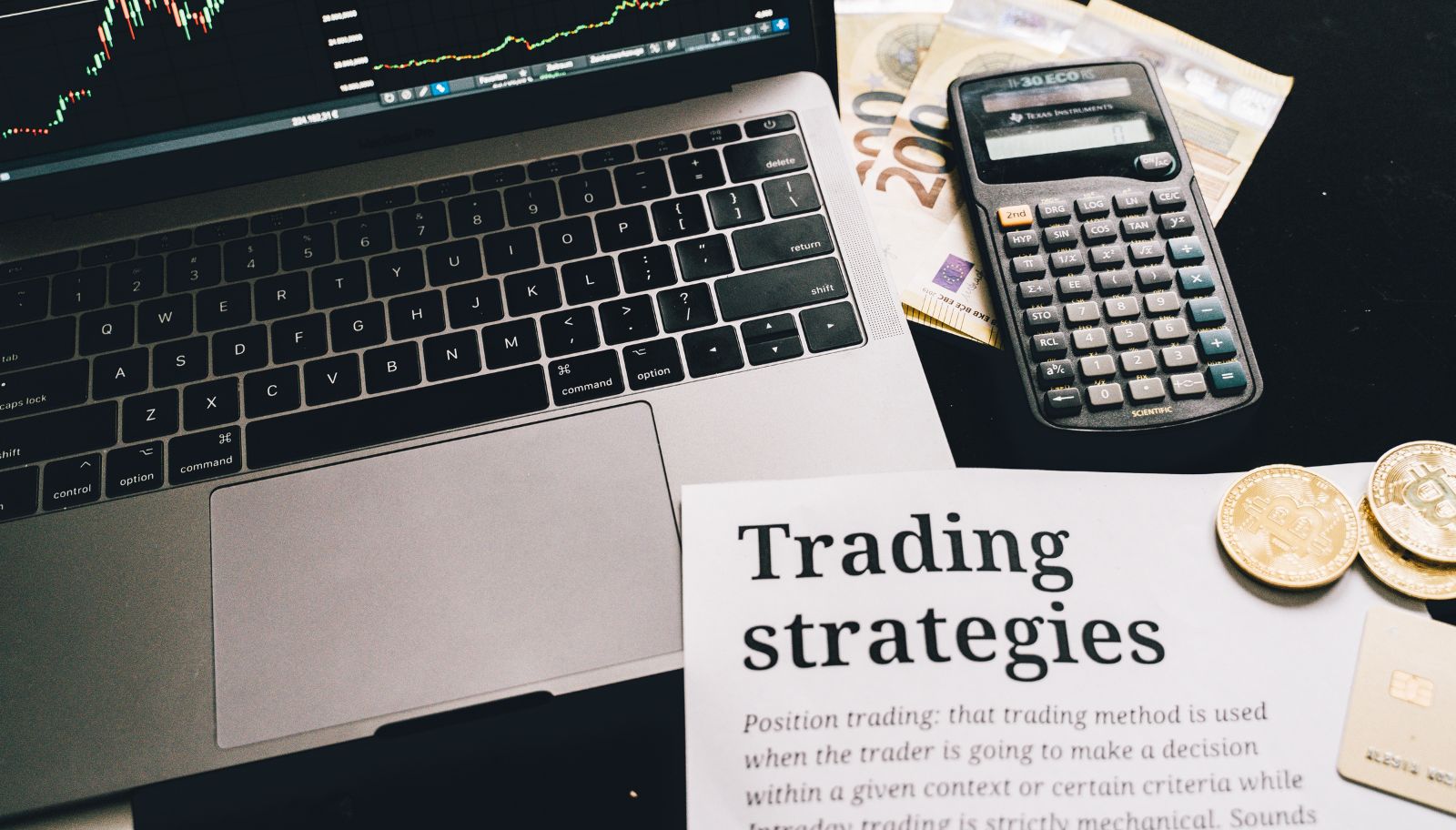 لابتوب يعرض شارت الأسهم مع ورقة تشرح استراتيجيات التداول وآلة حاسبة على مكتب تداول.
